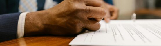 Close-up of an adult signing a legal document with a pen in an office.